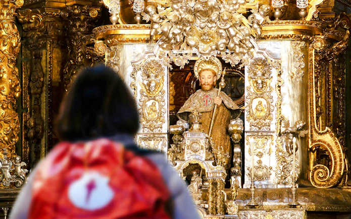 Pilgrim with backpack facing Apostle Santiago statue inside Santiago de Compostela Cathedral.