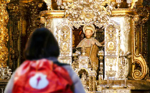 Pilgrim with backpack facing Apostle Santiago statue inside Santiago de Compostela Cathedral.