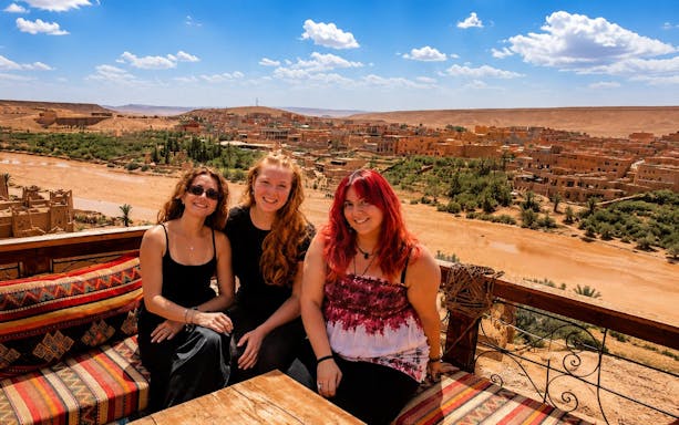 Scenic view of Aït Benhaddou village with three people seated in Marrakech, Morocco.