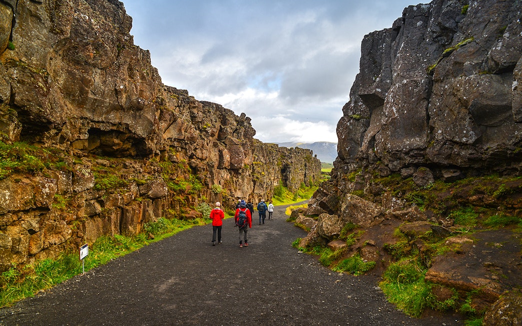 Tourists hiking through rocky landscape in Þingvellir National Park, Iceland.