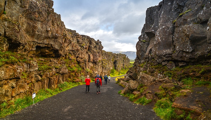 Tourists hiking through rocky landscape in Þingvellir National Park, Iceland.