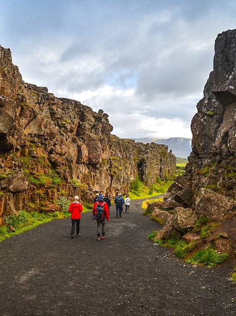 Tourists hiking through rocky landscape in Þingvellir National Park, Iceland.