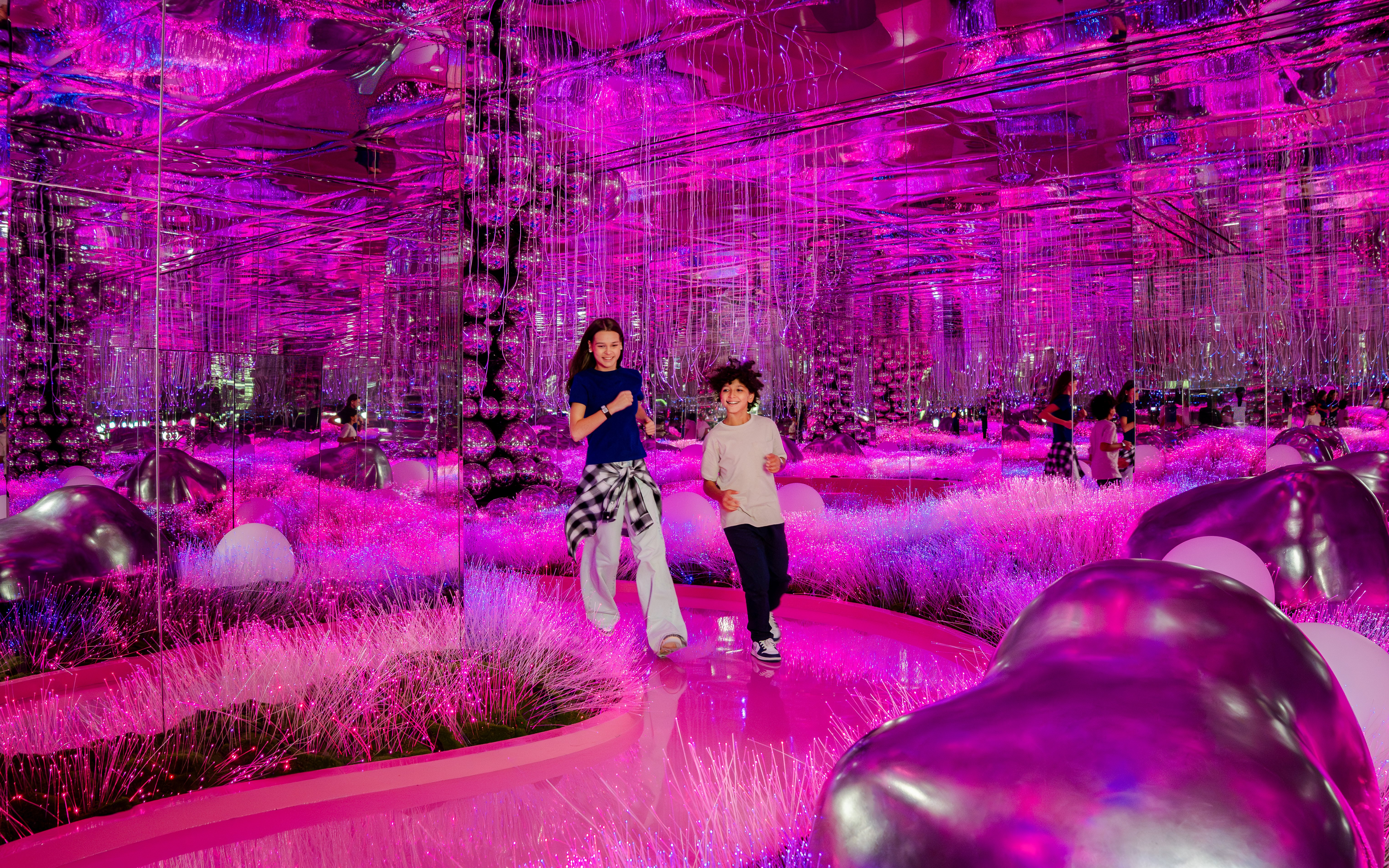 Visitors exploring vibrant pink mirrored room at House Of Hype exhibit.