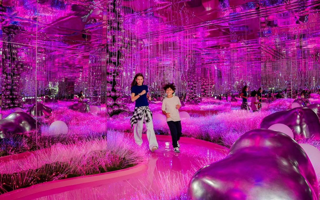 Visitors exploring vibrant pink mirrored room at House Of Hype exhibit.