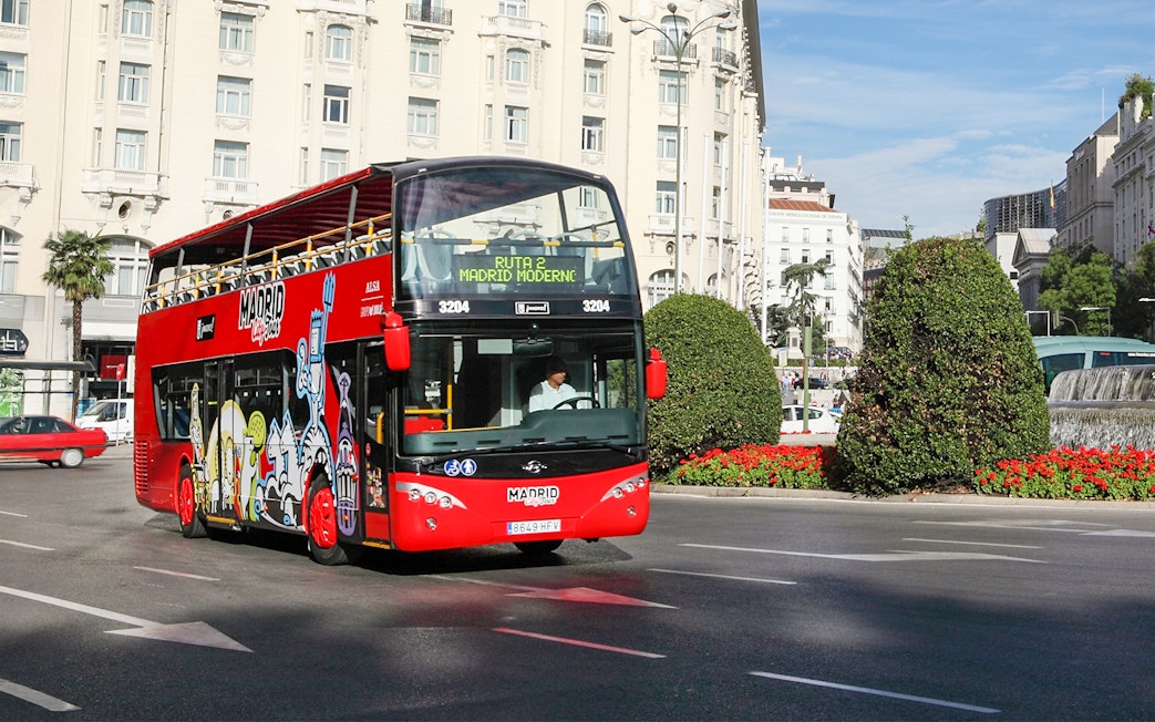 Red double-decker bus on Madrid city tour near historic buildings.