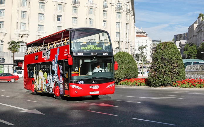 Red double-decker bus on Madrid city tour near historic buildings.