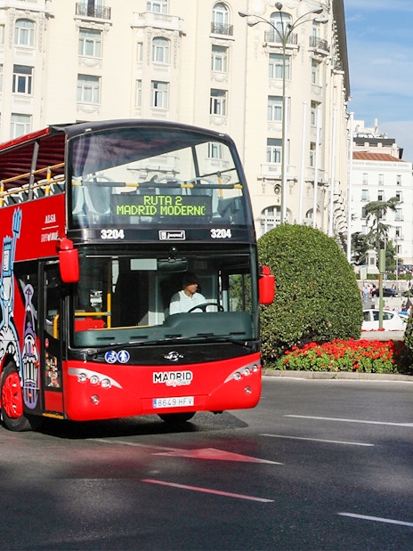 Red double-decker bus on Madrid city tour near historic buildings.