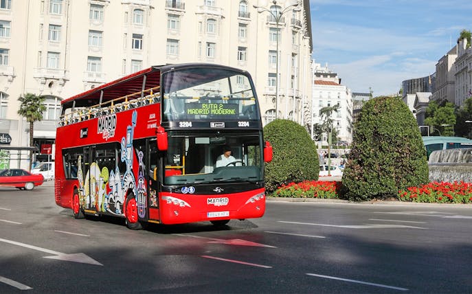 Red double-decker bus on Madrid city tour near historic buildings.