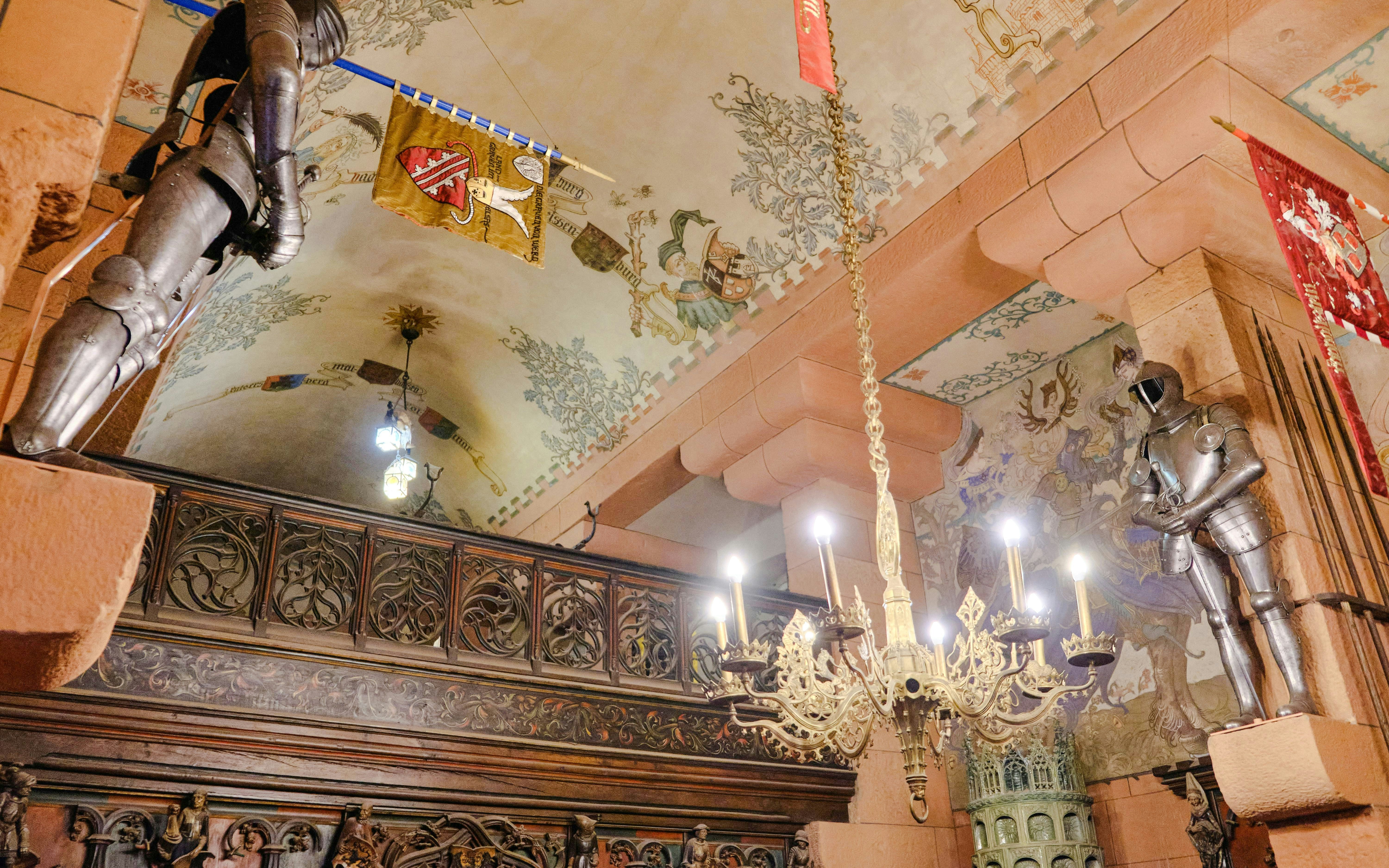 Knights' armor and ornate chandelier inside Haut-Koenigsbourg Castle, France.