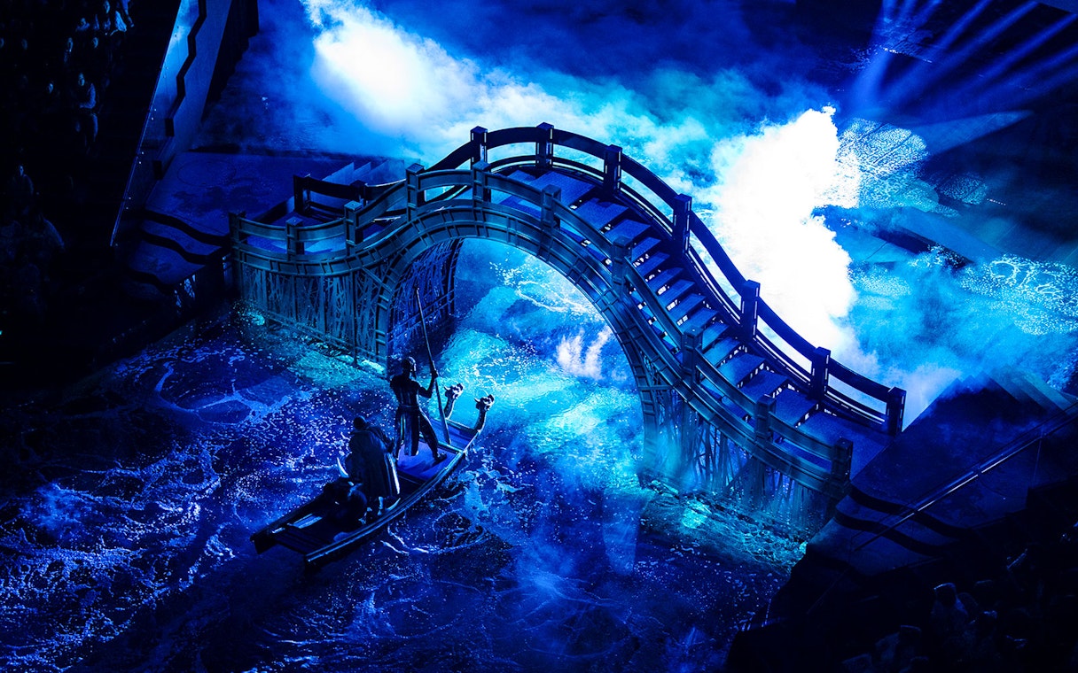 Boat under illuminated bridge during House of Dancing Water performance.