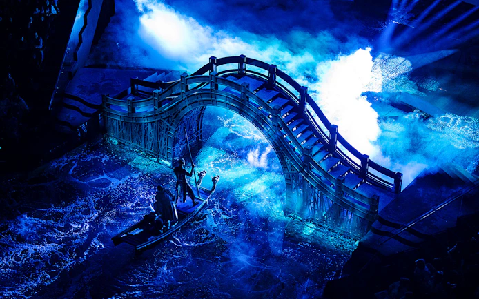 Boat under illuminated bridge during House of Dancing Water performance.