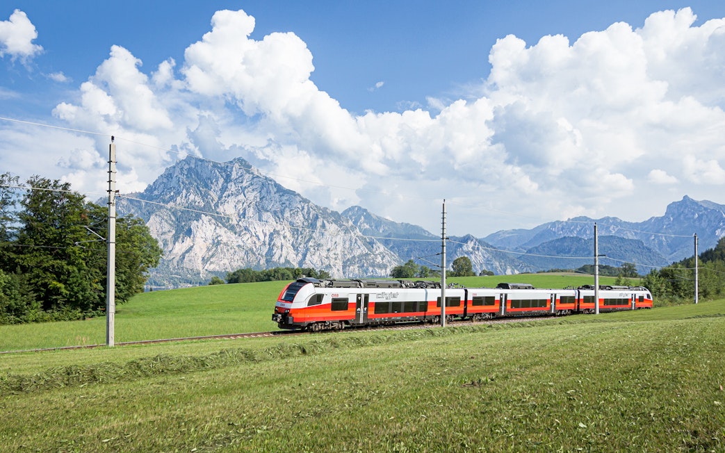 Train traveling through scenic European countryside with mountains in the background.