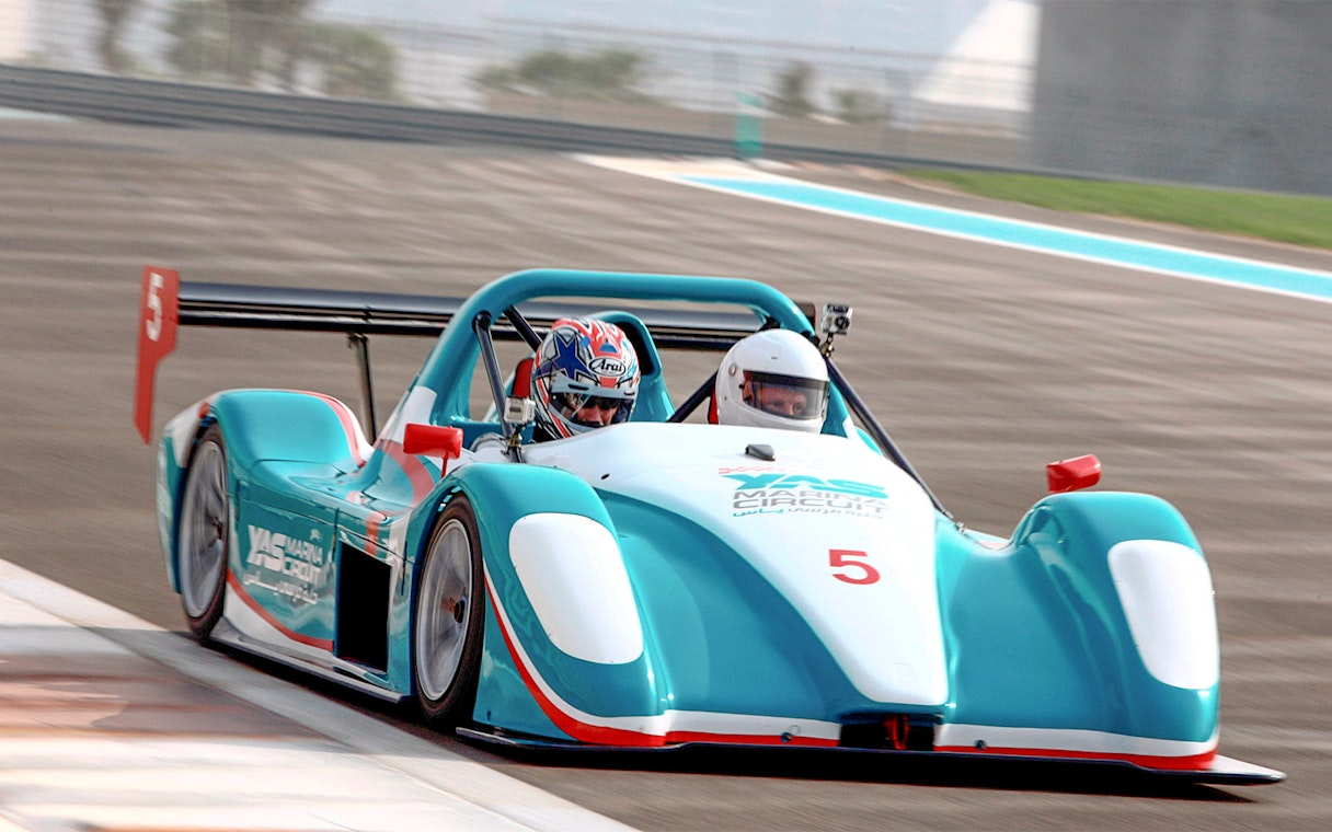 Racing car with two passengers on Yas Marina Circuit track.