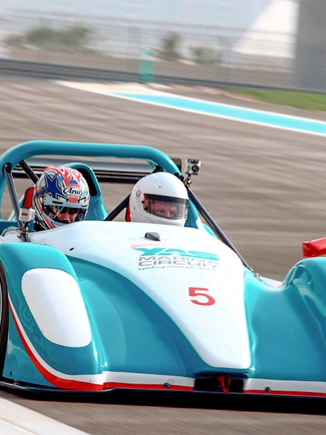 Racing car with two passengers on Yas Marina Circuit track.