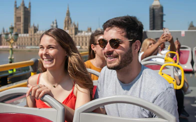 Passengers enjoying the view on a London hop-on hop-off bus tour with Big Ben in the background.