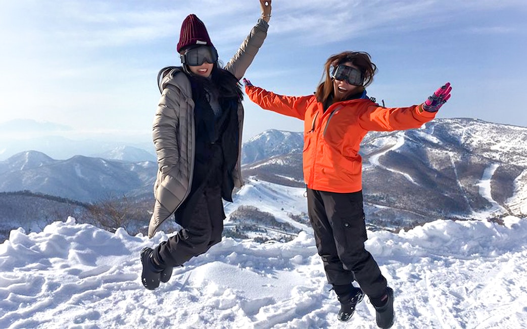 Tourists jumping joyfully in snowy Shiga Kogen with mountain views.