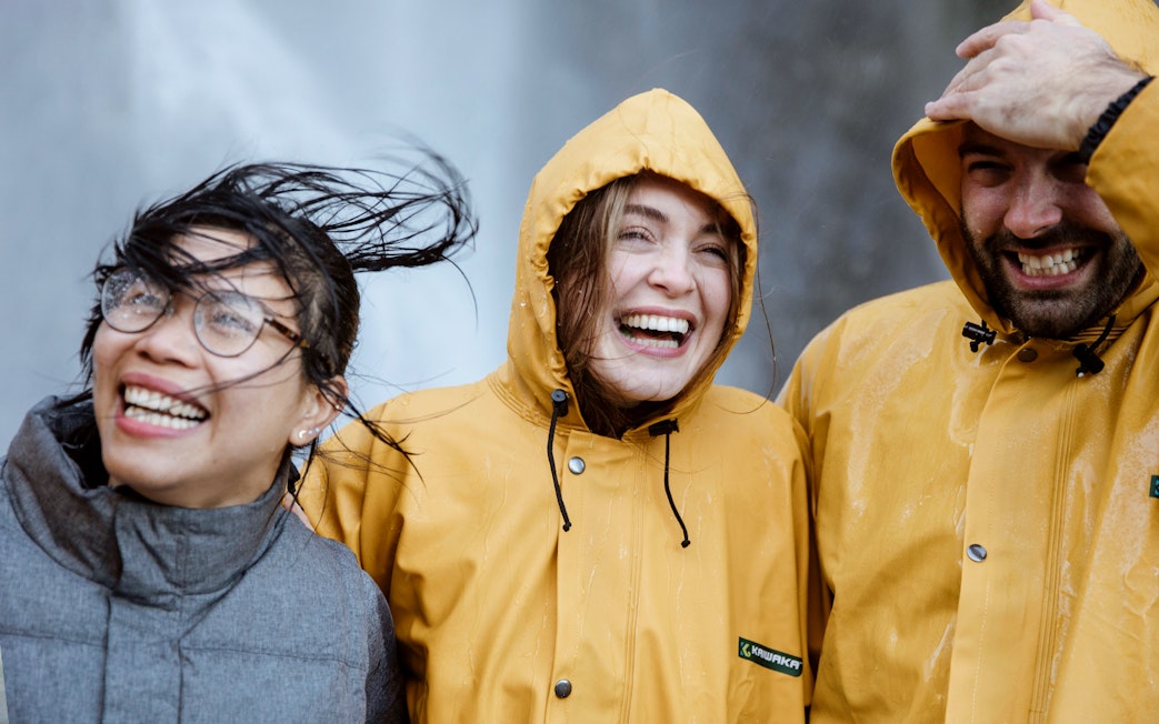 Tourists in raincoats smiling on a Milford Cruise day trip in New Zealand.