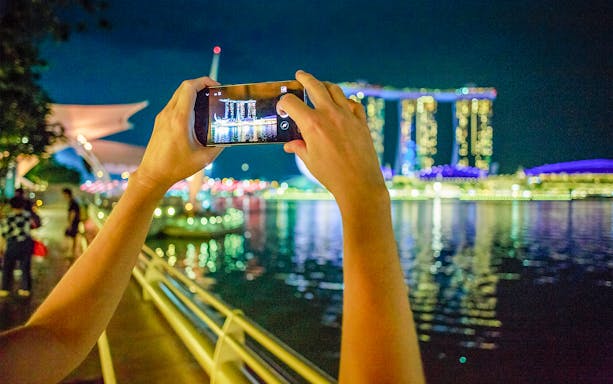 Hands holding a phone capturing Marina Bay Sands at night, Singapore.