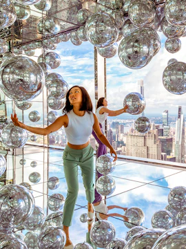 Visitors exploring mirrored room at Summit One Vanderbilt with New York City skyline views.