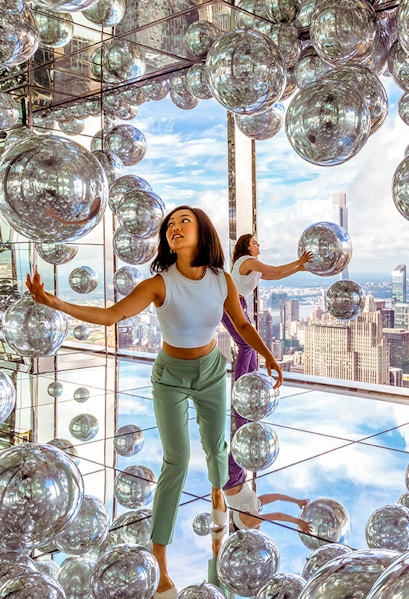 Visitors exploring mirrored room at Summit One Vanderbilt with New York City skyline views.