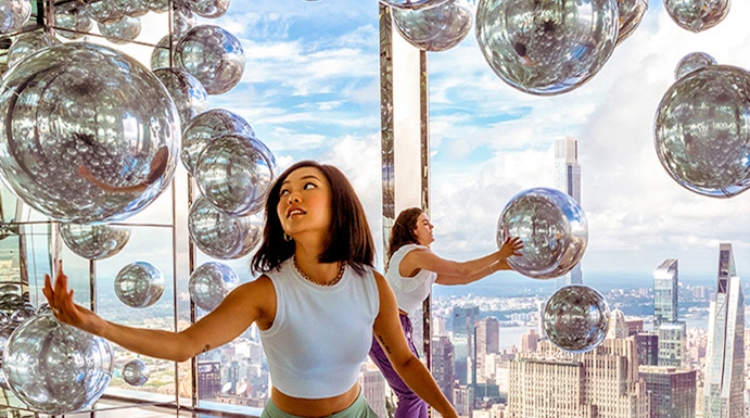 Visitors exploring mirrored room at Summit One Vanderbilt with New York City skyline views.