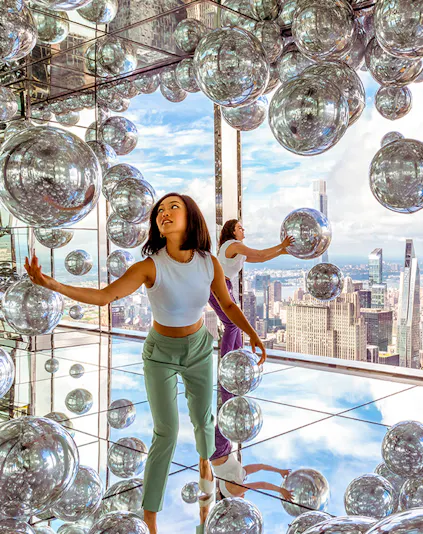 Visitors exploring mirrored room at Summit One Vanderbilt with New York City skyline views.