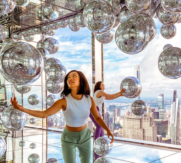Visitors exploring mirrored room at Summit One Vanderbilt with New York City skyline views.