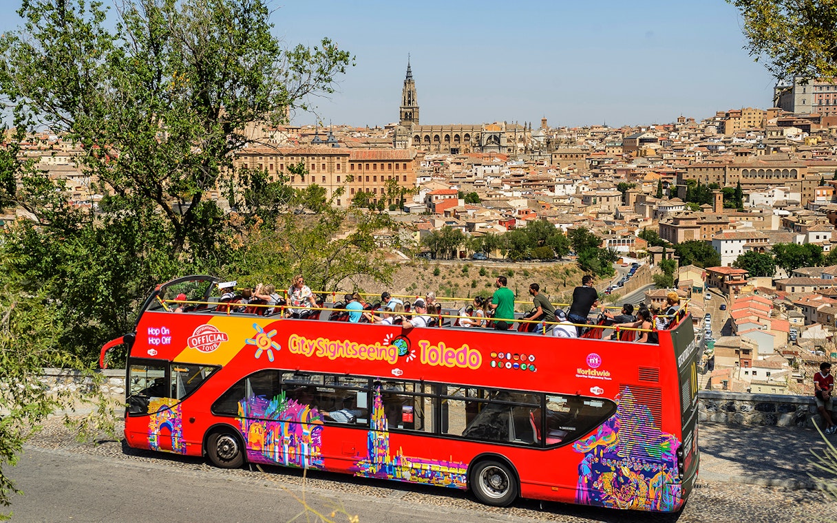 Toledo cityscape with tourists on a red hop-on-hop-off bus, featuring the Toledo Cathedral in the background.