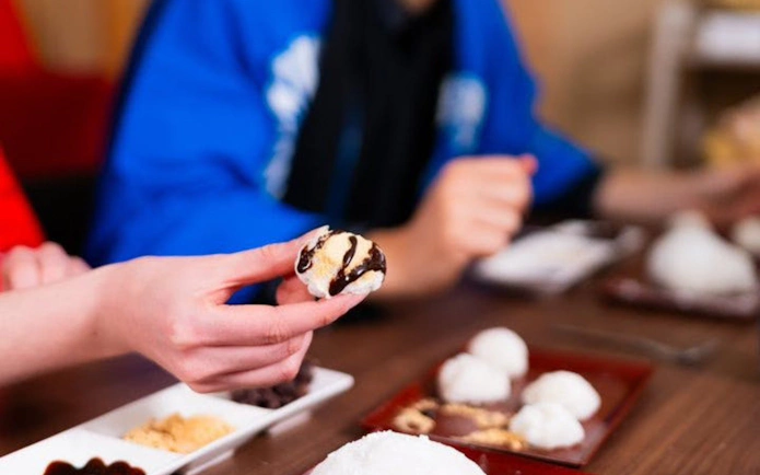 Hand holding mochi with chocolate drizzle during Kyoto mochi pounding experience.