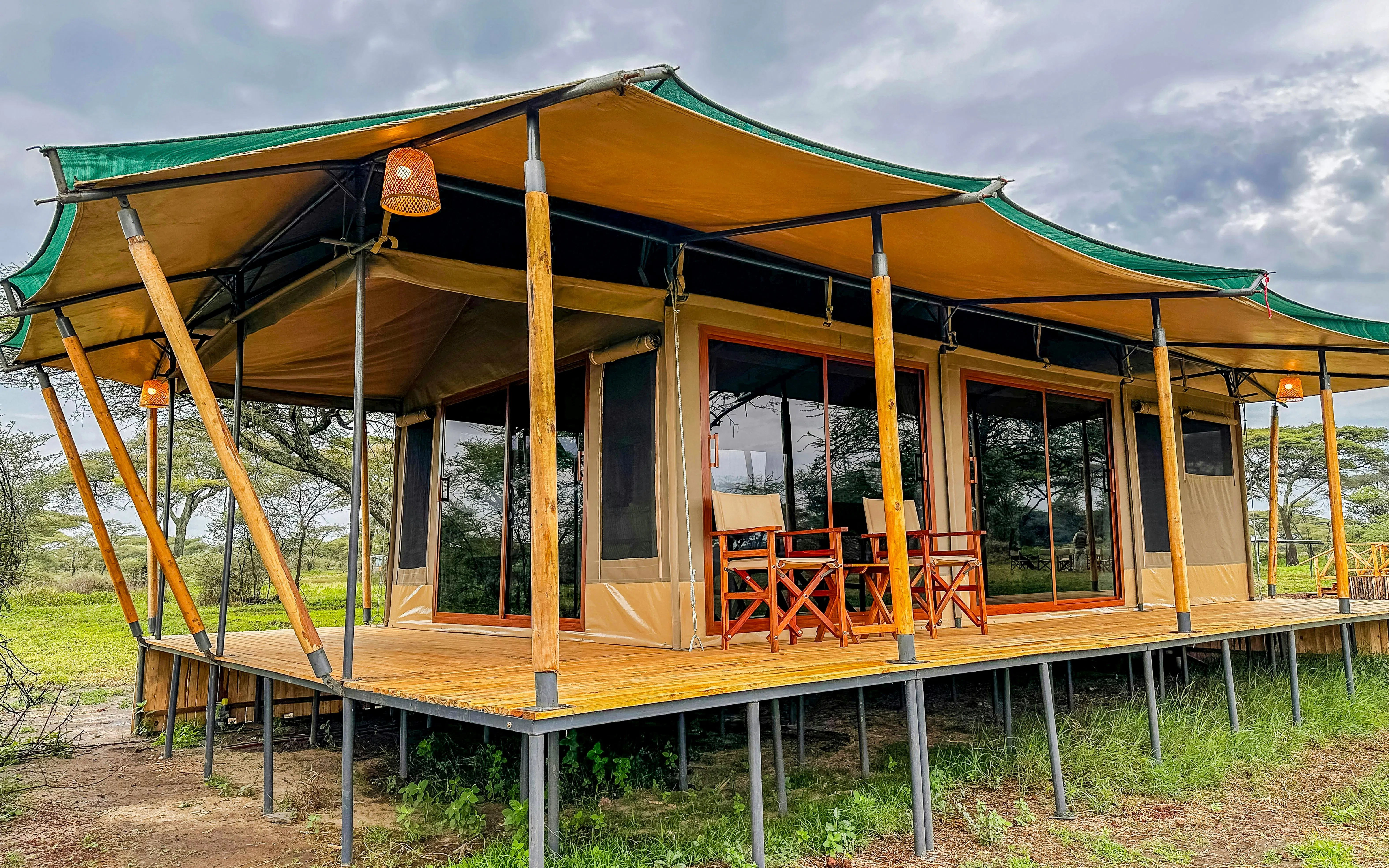 Luxury safari tent with wooden deck and chairs in African savanna.