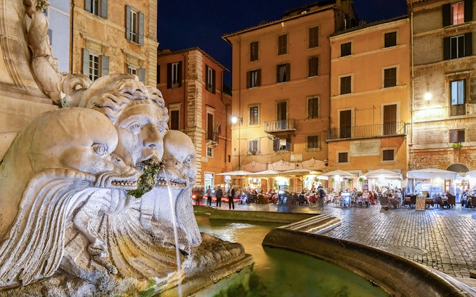 Pantheon Fountain at night with illuminated cafes and shops in Piazza della Rotonda, Rome, Italy.