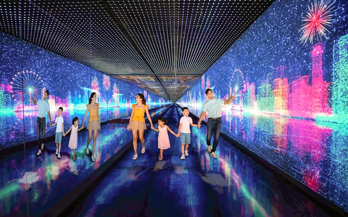Family exploring digital art tunnel at Singapore Flyer with cityscape and fireworks.