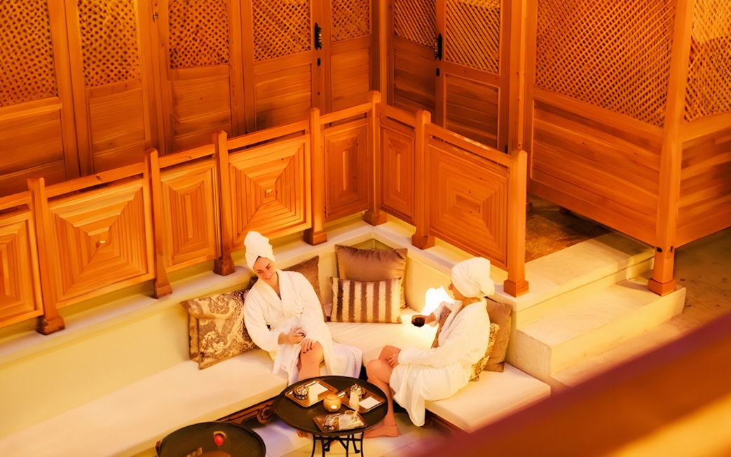 Two people relaxing in Hurrem Sultan Hamam, Istanbul, with wooden decor and cushions.