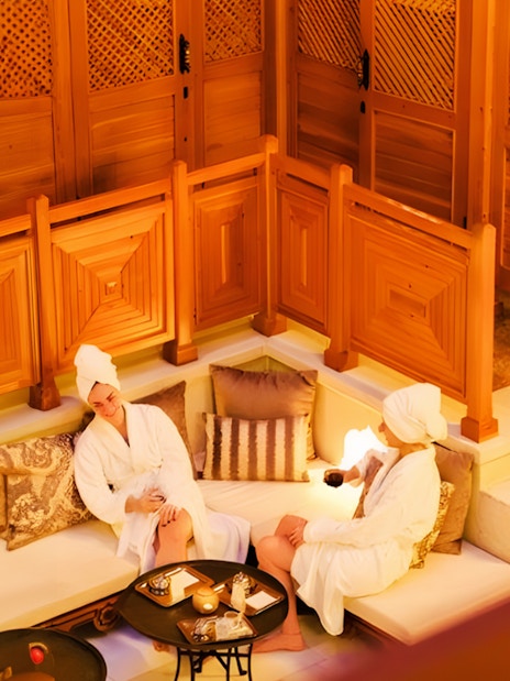 Two people relaxing in Hurrem Sultan Hamam, Istanbul, with wooden decor and cushions.