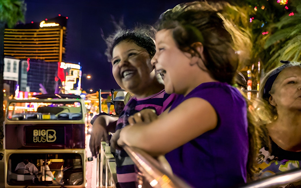Open-top bus tour at night in Miami with people enjoying city lights.