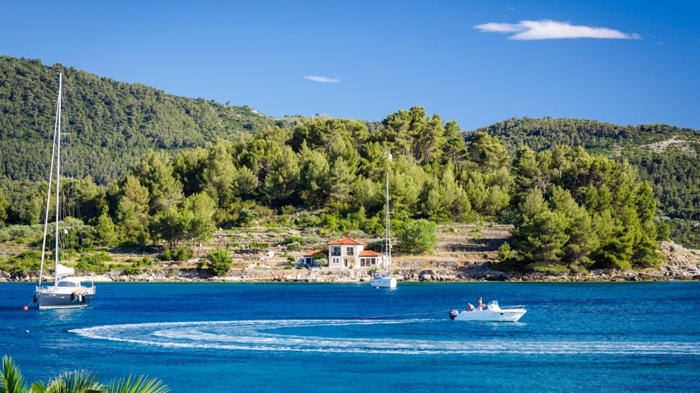 Sailboats and motorboat on the Blue Lagoon, Croatia, with lush green hills in the background.