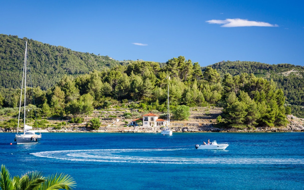 Sailboats and motorboat on the Blue Lagoon, Croatia, with lush green hills in the background.