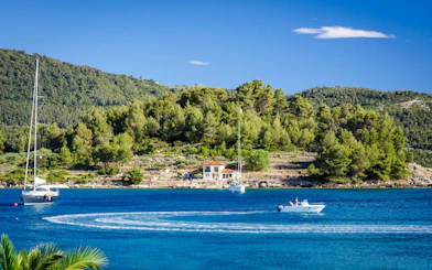 Sailboats and motorboat on the Blue Lagoon, Croatia, with lush green hills in the background.