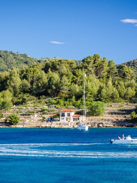 Sailboats and motorboat on the Blue Lagoon, Croatia, with lush green hills in the background.