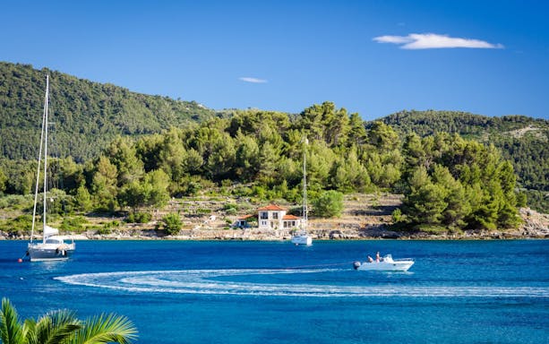 Sailboats and motorboat on the Blue Lagoon, Croatia, with lush green hills in the background.