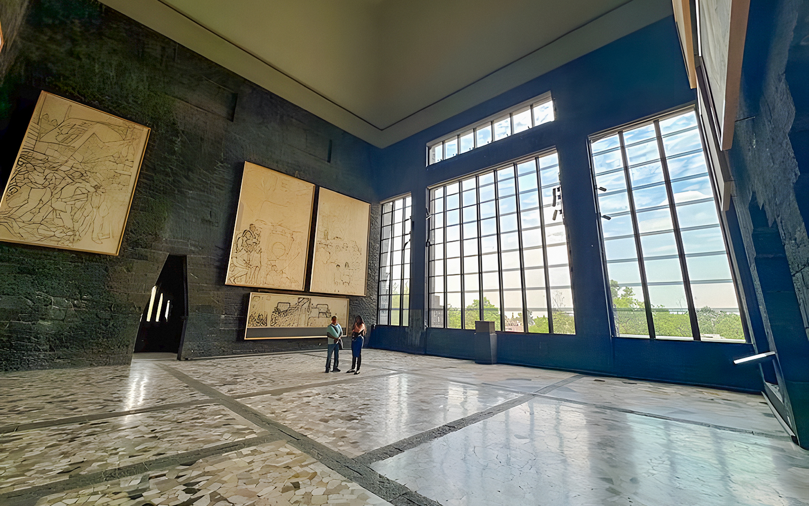 Interior of Anahuacalli Museum with large windows and mural art on dark stone walls.