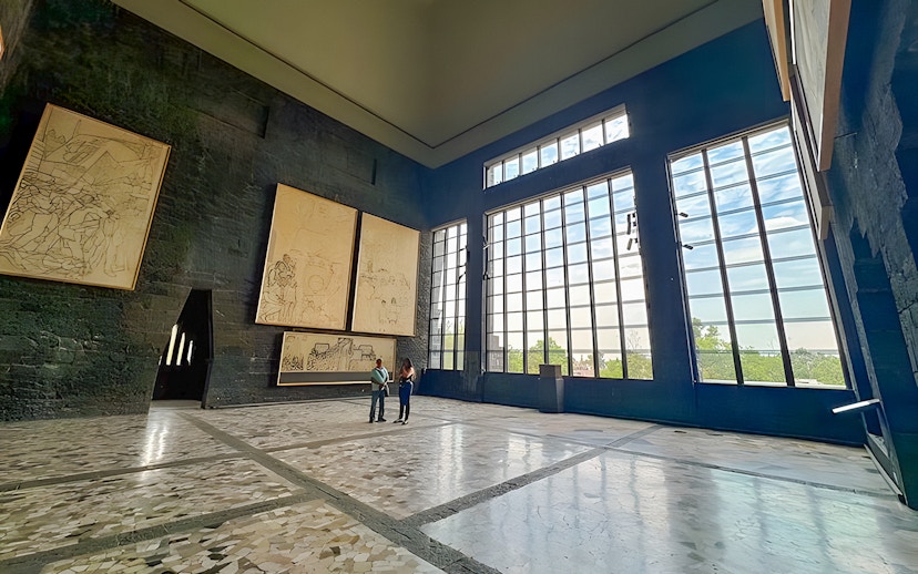 Interior of Anahuacalli Museum with large windows and mural art on dark stone walls.