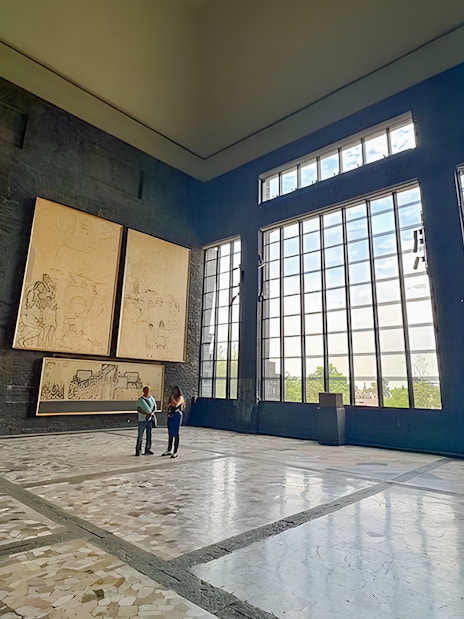 Interior of Anahuacalli Museum with large windows and mural art on dark stone walls.