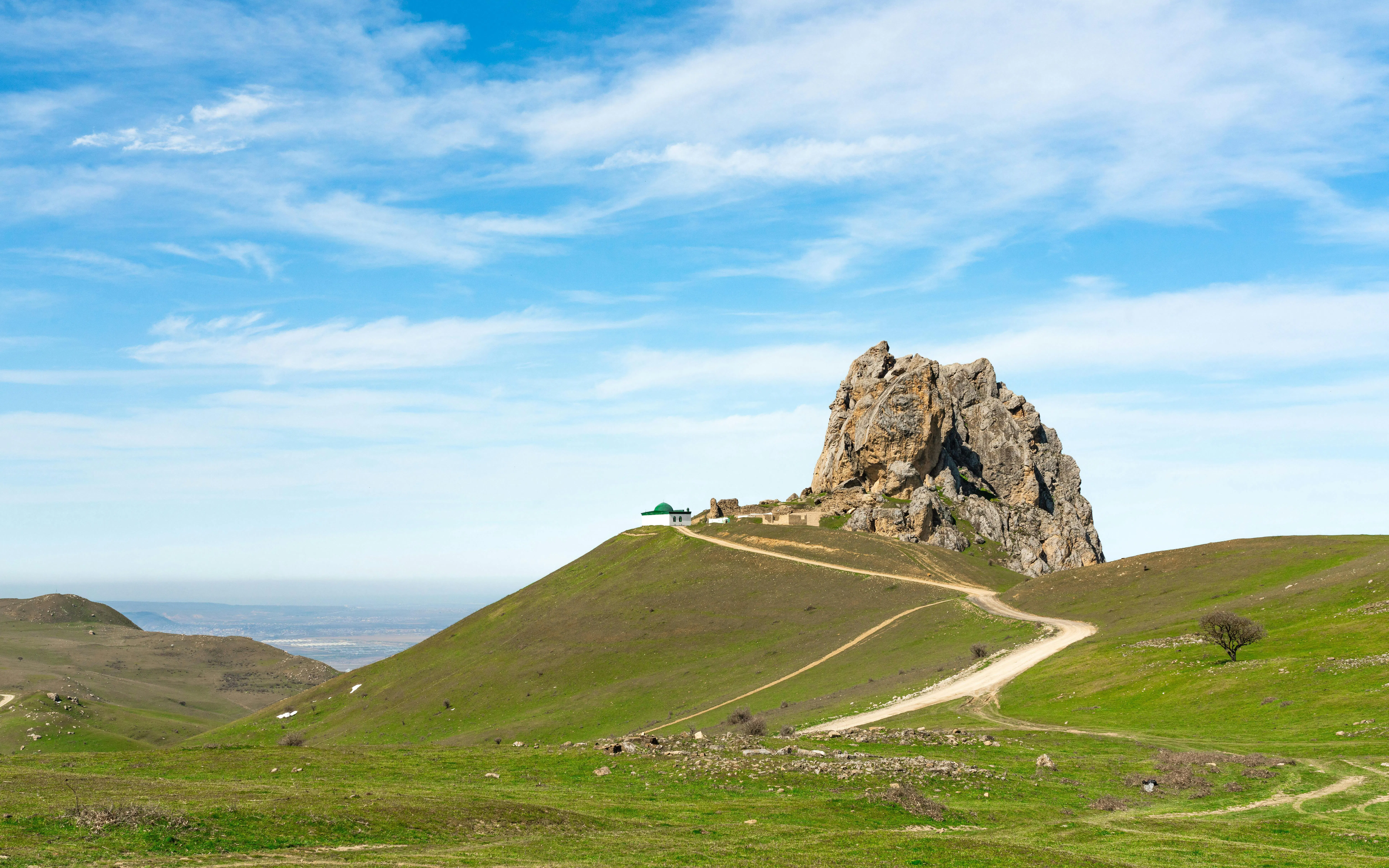 Rocky peak of Holy Mountain Beshbarmag in Azerbaijan with a winding path and green landscape.