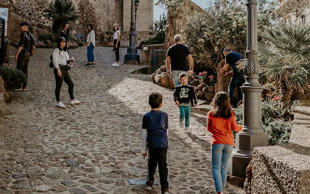 Tourists walking on a cobblestone street in Castelsardo, Sardinia, during a guided tour.