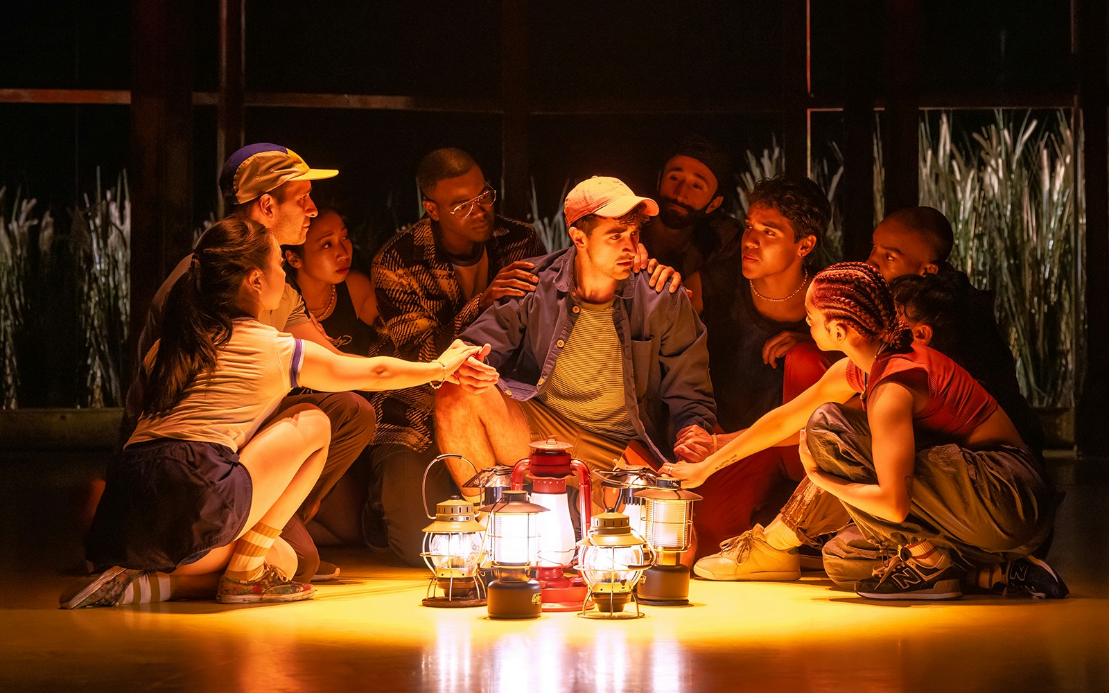 Group gathered around lanterns in a dimly lit setting, Illinoise tour experience.