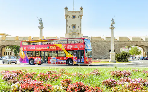 Hop-On Hop-Off Cadiz bus passing by historic city gate with statues.