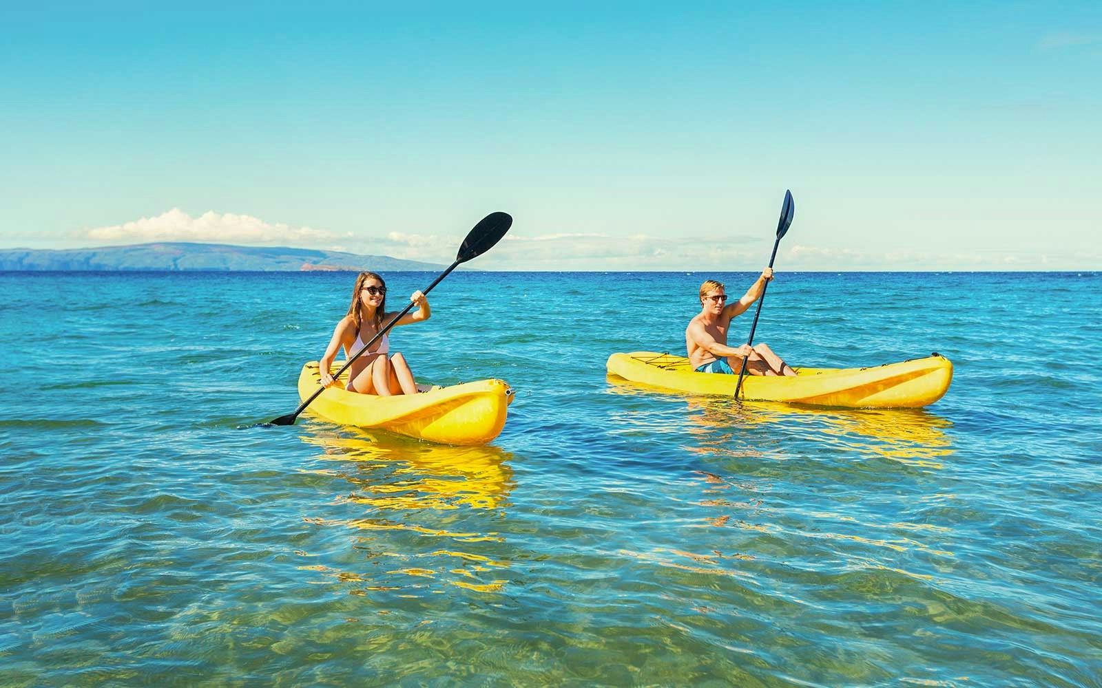 Couple kayaking on clear blue waters in Hawaii.