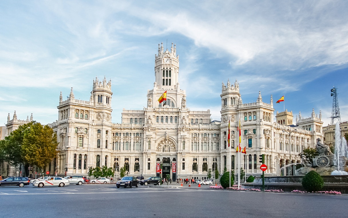 Cibeles Palace in Madrid with Spanish flags and fountain in foreground.