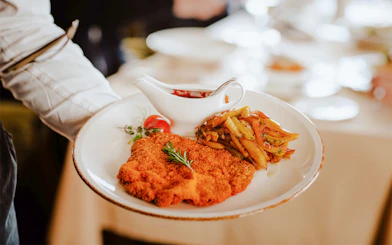 Waiter serving Viennese Schnitzel with fried potatoes and sauce.